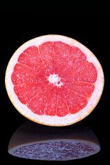 Half of citrus fruit of red grapefruit isolated on black background; close up