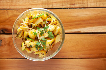 Close-up of Indian vegetarian classic dish Jeera Aloo - Potatoes Flavored with Cumin garnished with green coriander fresh leaves. Served in a glass bowl over wooden background