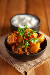 Close-up of Indian vegetarian dish of spicy Potato and Tomato curry garnished with green coriander fresh leaves with curd. over wooden background.