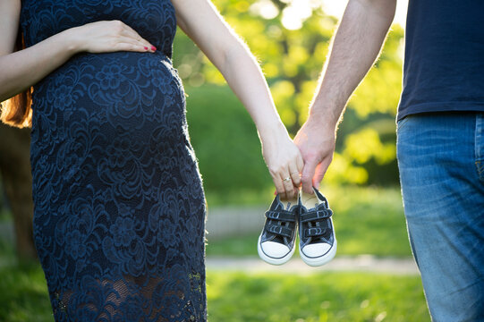 Schwangere Frau mit Partner h&auml;lt Babyschuhe &ndash; Vorfreude auf das Baby