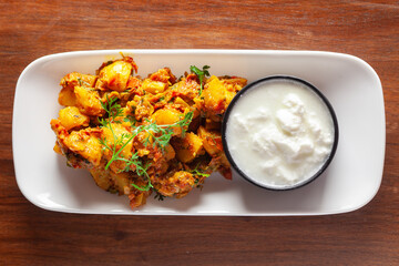 Close-up of Indian vegetarian dish of spicy Potato and Tomato curry garnished with green coriander fresh leaves with curd. over wooden background.