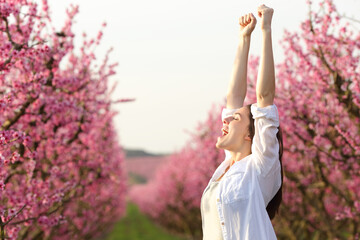 Excited woman raising arms celebrating spring in a field