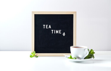 Tea time. Black letter board with text on table with glass cup of tea with mint leaves