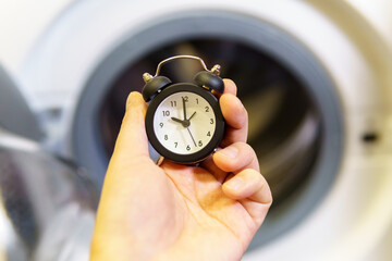 Washing clothes. Time to wash your dirty laundry. alarm clock in hand selective focus