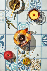 Fruit tea with apples and thyme in glass teapot and cup on table made of colored tiles
