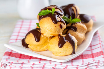 Delicious profiteroles with chocolate and white plate. Selective focus image on light background.