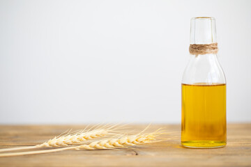 Oil from wheat in a bottle and wheat ears on a wooden table on a white background. Copy space.