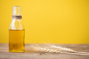 Oil from wheat in a bottle and wheat ears on a wooden table on a yellow background. Copy space.