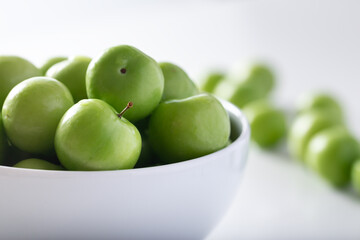 Fresh green plums in white bowl. 