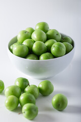 Fresh green plums in white bowl. 