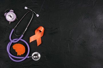 Orange awareness ribbon, brain symbol, stethoscope and alarm clock on a black background. Copy...