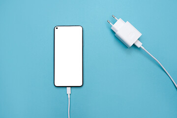 Smartphone charging connection via USB cable and power supply on a blue background. Smartphone with...
