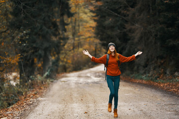 happy woman hiker with backpack walks on the road in autumn forest