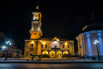 Naklejka premium The old town hall in Kamianets-Podilskyi illuminated by lanterns at night. Beautiful town hall with clock in the historical part of Kamianets-Podilskyi