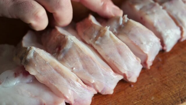 Close up shot of slices of monkfish arranged on a cutting board. One hand touches and checks the slices. Mediterranean diet, food and health concept.