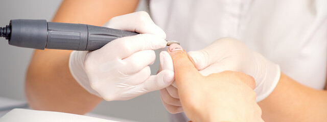 Manicure master applying electric nail file machine removing old nail polish on fingernails in a nail salon