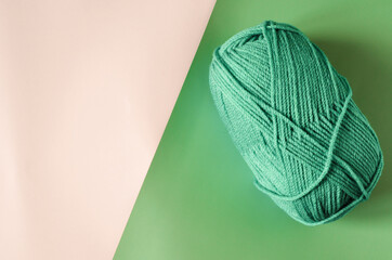 A ball of green yarn on a colored beige-green background close-up, knitting concept.