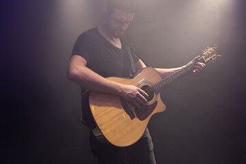 Guitarist playing acoustic guitar in a dark smoky room.