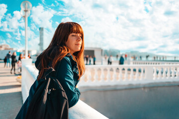 Obraz premium Vacation at the sea. A portrait of a beautiful woman leaning on a balustrade, basking in the sun with her eyes closed. Promenade