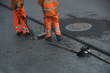 Arbeiter im Straßenbau fegt mit Besen Kanaldeckel frei von Asphalt