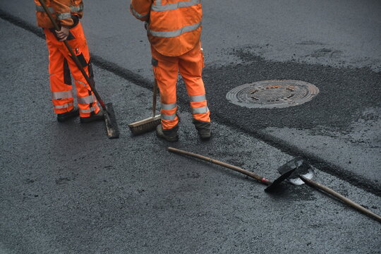 Arbeiter im Stra&szlig;enbau fegt mit Besen Kanaldeckel frei von Asphalt