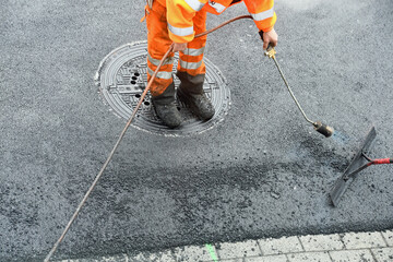 Straßenarbeiter erhitzt mit Brenner Asphalt beim asphaltieren
