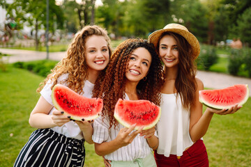 Three young woman relaxing on the grass and eating watermelon.  People, lifestyle, travel, nature and vacations concept.