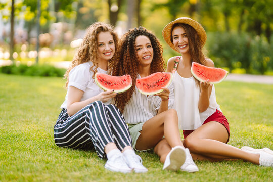 Three young woman relaxing on the grass and eating watermelon.  People, lifestyle, travel, nature and vacations concept.