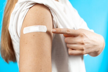 After vaccination. Close-up, hand with a plaster after the injection on blue background.