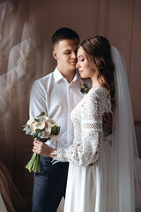 Wedding portrait of the bride and groom in a lace dress with a bouquet.