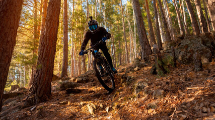 A man on a bicycle through the forest from a mountain on a bright sunny day. The guy rides through the trees. Cyclists riding a mountain electric bicycle steep uphill in harsh rocky terrain