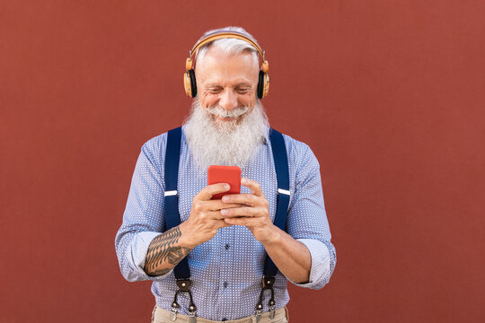 Senior hipster man using mobile smartphone while listening music playlist outdoors in city - Elderly people lifestyle and tech concept