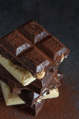 Stack of milk and dark chocolate with nuts, caramel and fruits and berries on dark marble...