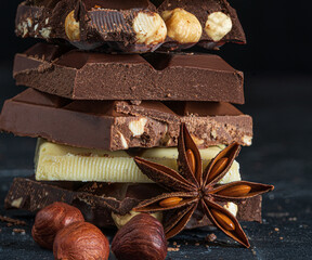 Stack of milk and dark chocolate with nuts, caramel and fruits and berries on dark marble background..