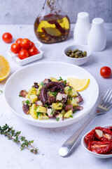 Warm salad with octopus, potatoes, tomatoes, capers and lemon on a white plate. Close-up, white background.