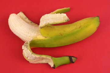 Banane à moitié épluchée en gros plan sur fond rouge