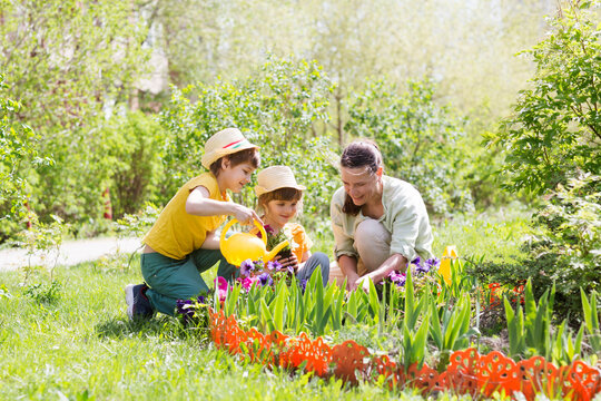 mother and two kids plant flowers in the garden near the houme on spring day. children help mom work in the garden. slow life. enjoy the little things. 