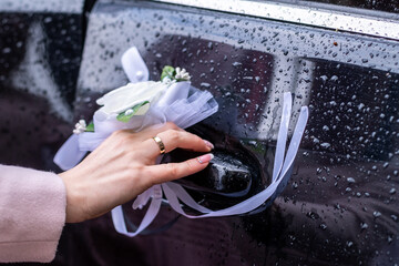Female hand with wedding ring open car door handle in the rain.