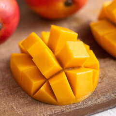 Diced fresh mango fruit on wooden cutting board with sunlight and leaf shadow.