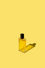 transparent perfume bottle with liquid stands in the sunlight with shadow on yellow background