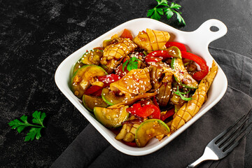 Traditional asian dish squid with vegetables in sweet and sour sauce on a black background close up