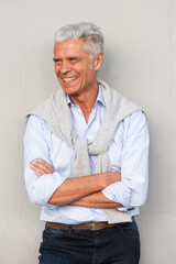smiling older man with arms crossed by white wall looking away