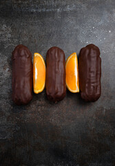 Traditional French eclairs with orange slices on a dark grey background .