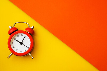 red analog alarm clock on two tone, yellow and orange, paper background, top view