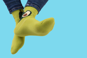 legs dangling down, wearing green socks with avocado pattern, on turquoise background