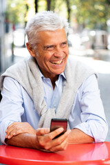 Obraz premium Close up smiling older man sitting at table with cellphone in hand