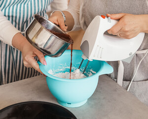 Two girls are preparing homemade marshmallows together. One whips with a mixer, the second pours in jam
