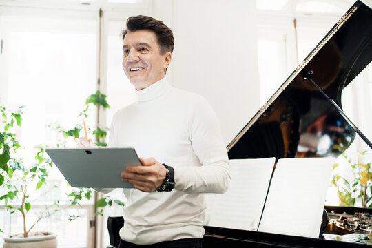 The artist works at home and plays the piano. Favorite activity of an adult. He teaches at a music school. A male adult musician writes down the notes in a tablet for a new song.