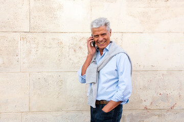 Fototapeta na wymiar Side of smiling older man talking with mobile phone by white wall