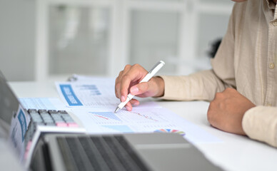 Cropped shot of Hand pointing pen to graph data on the desk with calculator and laptop,Business concepts.